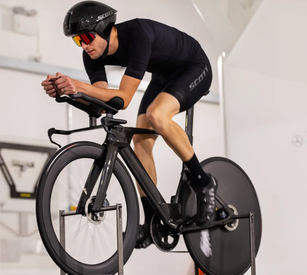 Radfahrer in Aeroposition auf schwarzem Zeitfahrrad (Scott), Aerohelm und Brille im Windkanal-Test