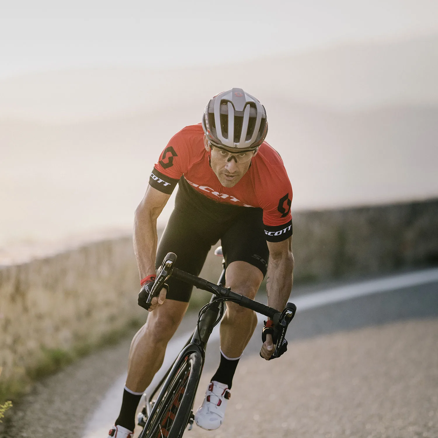 Großer Radfahrer in rotem Trikot und Helm beim Kurvenfahren auf Rennrad, Blick nach vorn, Radsport/Performance