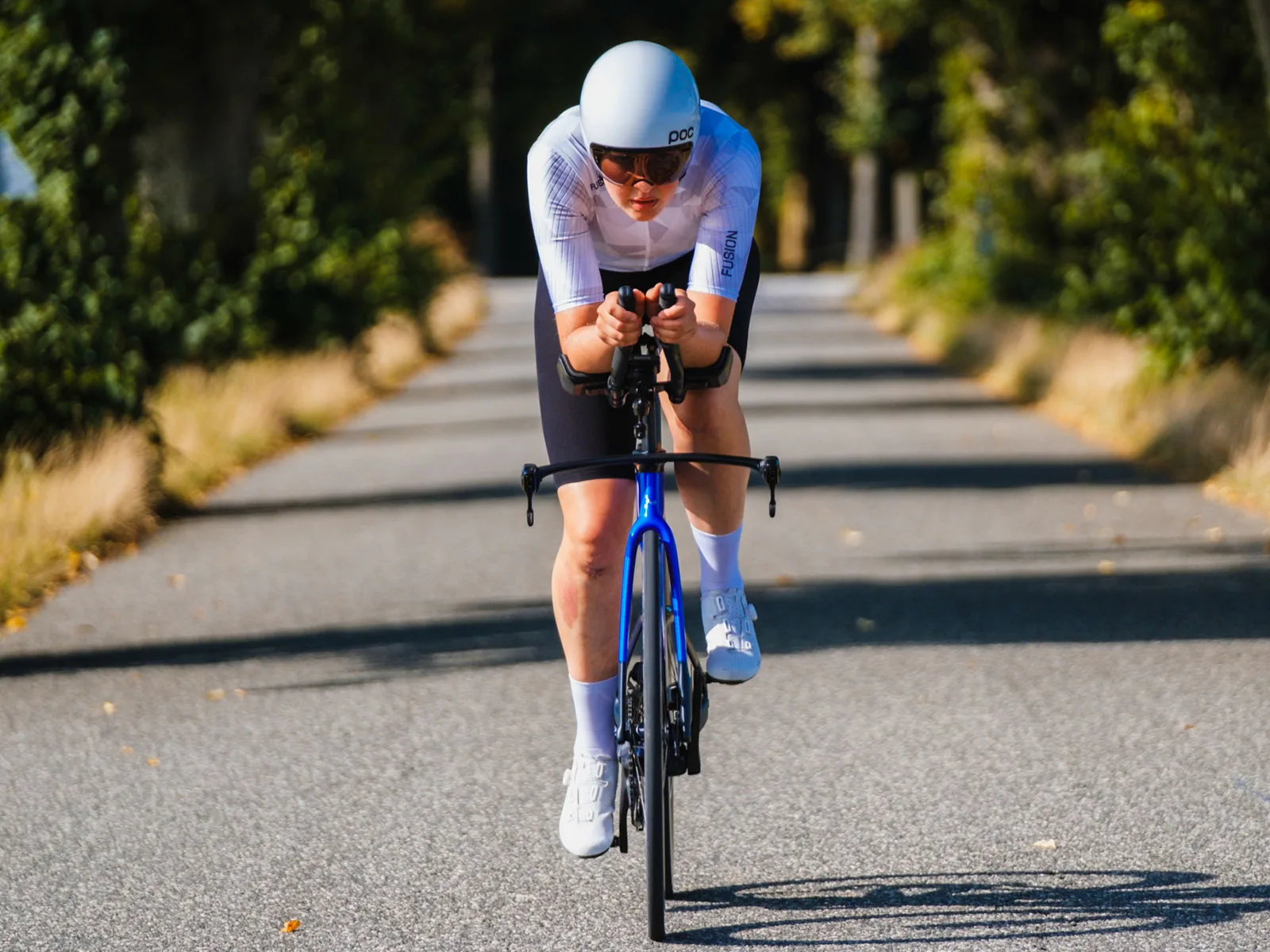 Triathletin auf blauem Rennrad in Aeroposition auf sonniger Landstraße, Rennrad, Zeitfahr-Helm und Sportbekleidung